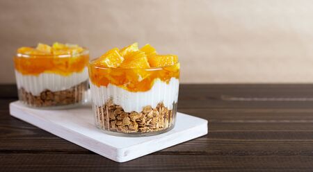 Dessert of yogurt, jam, orange and granola on a brown wooden table. Healthy food. Breakfast. Banner with copy space.の写真素材