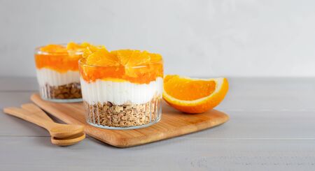 Breakfast of yogurt, jam, orange and granola on a gray wooden table. Healthy food. Dessert. Banner with copy space.の写真素材