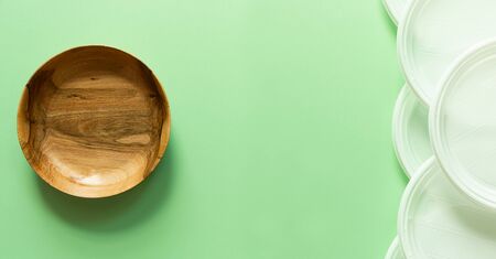 One wooden plate vs plastic plates on a green background. Zero waste. Save environment concept.の写真素材