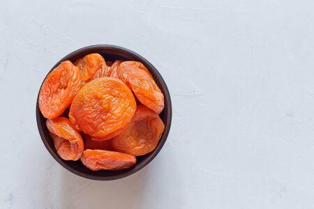Dried apricots in a brown clay bowl on a gray table. Top view, copy space.の写真素材