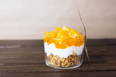 Dessert of yogurt, jam, orange and granola on a brown wooden table. Healthy food. Copy space.の写真素材