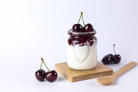 Dessert of natural yoghurt, jam and cherries on a white background. Healthy, delicious breakfast. Portion dessert in glassの写真素材