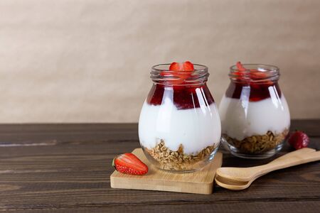 Jars of granola with yogurt, strawberry jam and fresh strawberries on a brown wooden table with copy space. Healthy, delicious breakfast.の写真素材