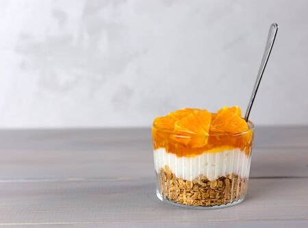 Dessert of yogurt, jam, orange and granola on a gray wooden table. Healthy, delicious breakfast. Copy space.の写真素材