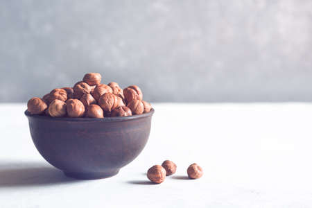 Hazelnuts in a brown clay bowl on a gray background with copy space. Healthy food.の写真素材