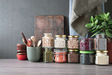 Beans, seeds and cereals in glass jars on a wooden table. Healthy food.の写真素材