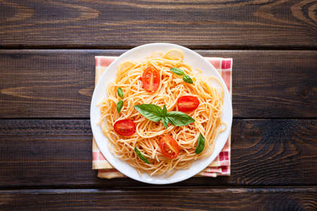 Pasta with cherry tomatoes, cheese and basil on a wooden background. Top view, copy space.の写真素材