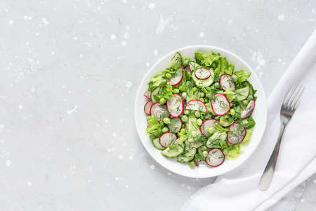 Fresh salad of cucumbers, radishes, green peas and herbs in white bowl. Top view.の写真素材