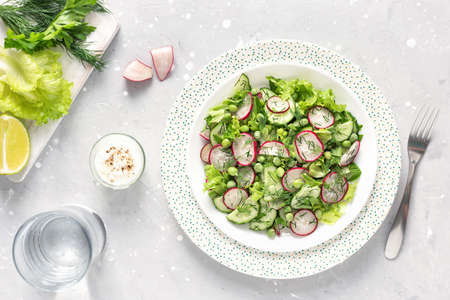 Fresh salad of cucumbers, radishes, green peas and herbs in white bowl. Flat lay. Diet food concept. Vegetarian and vegan foodの写真素材