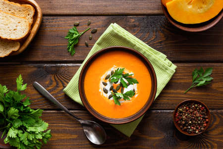 Pumpkin cream soup, served with crackers and parsley on a wooden table. Vegetarian and vegan food. Healthy eating.の写真素材