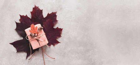 A gift box decorated with acorns lies on maple leaves. The concept of thanksgiving. Autumn background. Banner, top view, copy spaceの写真素材
