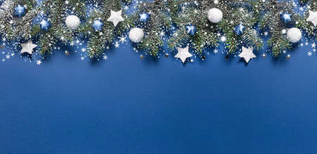 Christmas snowy border of shiny balls and stars, evergreen branches on classic blue background. New Year card, banner.の写真素材
