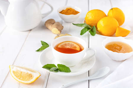 Antioxidant healthy tea with lemon, ginger, honey, turmeric and mint on a white wooden table. The concept of alternative medicine.の写真素材