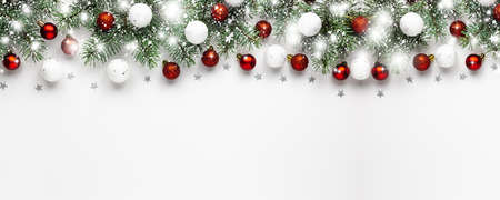 Christmas snow border of shiny white and red balls, evergreen branches on a white wooden background. New year card, banner.の写真素材