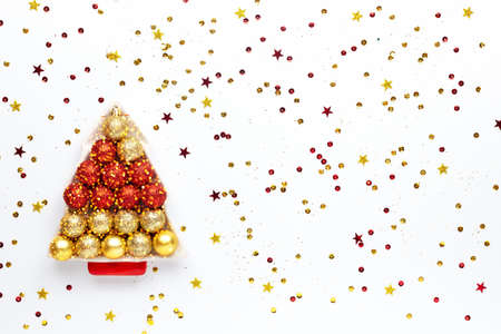 Christmas plate in the shape of a Xmas tree with toys, bokeh lights on a white wooden background strewn with confetti. New year greeting card. Copy space. Top view.の写真素材