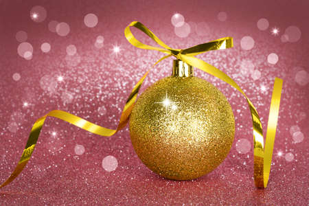 Golden Christmas ball on a pink sparkling background with bokeh lights. New year card. Shiny texture.の写真素材