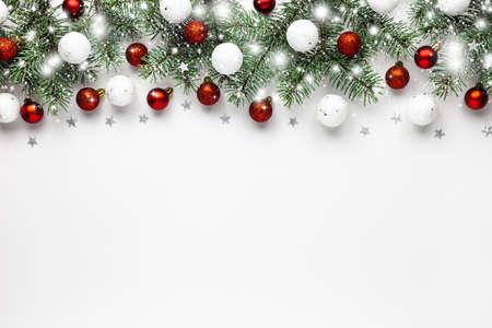 Christmas snow border of shiny white and red balls, evergreen branches on a white wooden background. New year card.の写真素材