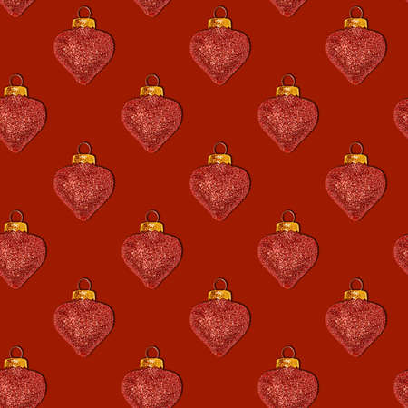 Seamless Christmas pattern with decorative shiny toys in the shape of a heart on a red backgroundの写真素材