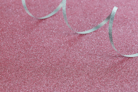 Christmas silver gift ribbon on a pink sparkling background. New year card. Shiny texture. Selective focus.の写真素材