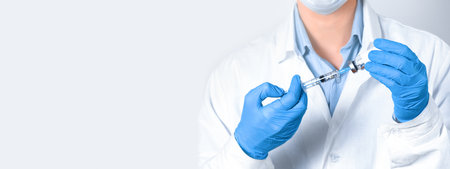A doctor, nurse, or scientist holds a vaccine and a syringe in blue gloves. The concept of medicine. Banner, copy spaceの写真素材