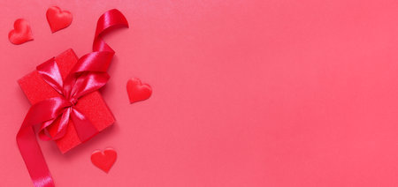 Red gift box tied with a ribbon with decorative hearts on a red background. Gift for Valentine's Day, Birthday, Mother's Day or International Women's Day. Bannerの写真素材