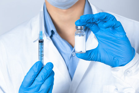 A doctor, nurse, or scientist holds a vaccine and a syringe in blue gloves. The concept of medicine.の写真素材