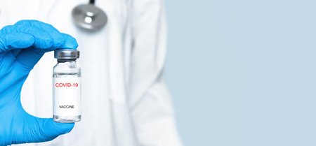 vaccine in a glass bottle in the hand of a doctor in a blue glove. The concept of a vaccine. Banner.の写真素材