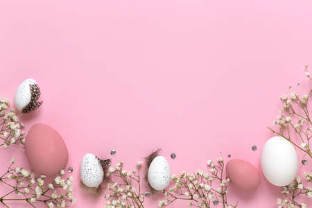 Easter eggs and spring flowers on a pink pastel background with copy space, flat lay.