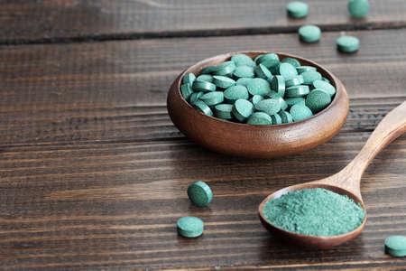 Green algae in powder and pills - chlorella, spirulina on a wooden background. Healthy green food supplement conceptの写真素材