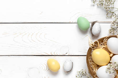 Easter background with colorful eggs in a basket on a white wooden background. Top view with copy spaceの写真素材