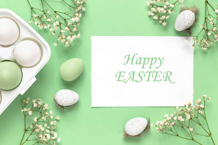 White and green Easter eggs, spring flowers on a green background. Flat lay, copy space. Easter decoration, modern design template.の写真素材