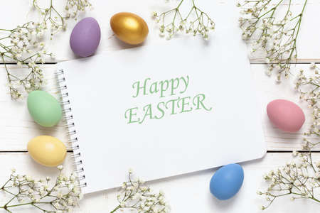 Easter background with colorful eggs and spring flowers on a white wooden background. Top view with copy space, mockup.の写真素材