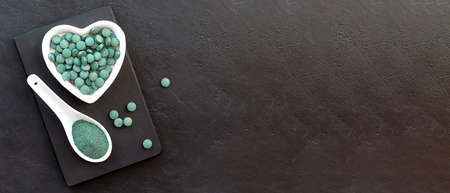 Green algae in powder and pills - chlorella, spirulina a black background. Healthy green food supplement concept.の写真素材