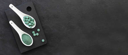 Green algae in powder and pills - chlorella, spirulina in white spoons on a black backgroundの写真素材