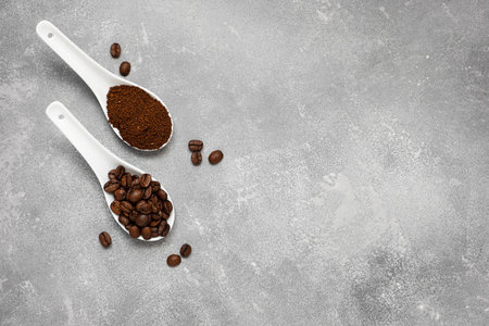 White porcelain spoons with coffee beans and ground coffee on a gray table. Top view, copy spaceの写真素材