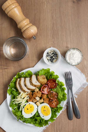 Caesar salad with fried chicken, fresh tomatoes, croutons, lettuce, parmesan cheese and eggs. Healthy eating. Top view.の写真素材