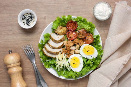 Caesar salad with fried chicken, fresh tomatoes, croutons, lettuce, parmesan cheese and eggs on a wooden tableの写真素材