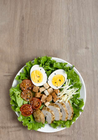 Caesar salad with fried chicken, fresh tomatoes, croutons, lettuce, parmesan cheese and eggs on a wooden table.の写真素材