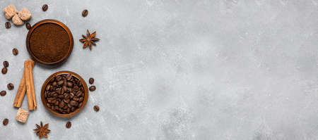 Coffee beans, ground coffee, brown sugar cane, star anise and cinnamon in wooden bowls on a gray background. Top view, copy space. Bannerの写真素材