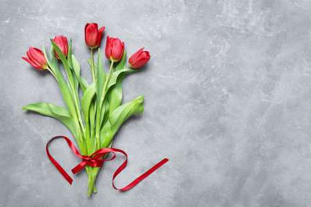 A spring bouquet of red tulips with a ribbon lay flat on the gray table. Festive background.の写真素材