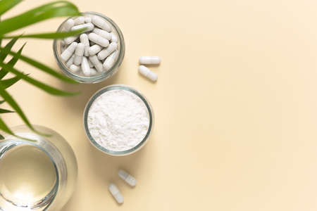 Collagen powder, tablets and a glass of water on a beige background with a copy space. Extra protein intake. Natural beauty and health supplement. Flatlay, top view.の写真素材