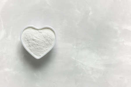 Collagen powder in a white heart-shaped cup on a gray background with a copy space. Natural supplement for beauty and healthの写真素材