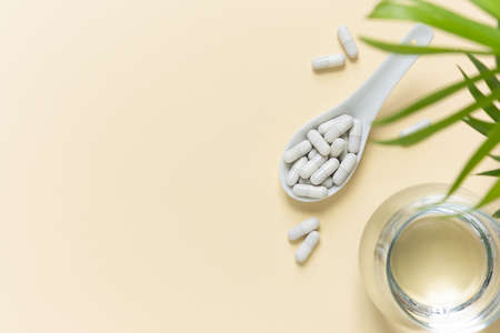 Collagen pills in a spoon and a glass of water on a beige background with a copy space. Extra protein intakeの写真素材