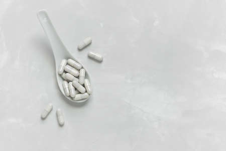 Collagen pills in a white spoon on a gray background with a copy space. Natural supplement for beauty and health.の写真素材