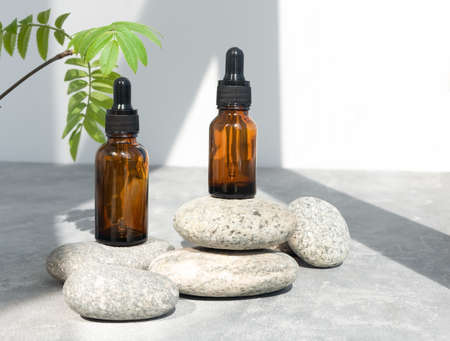 Bottles of dark amber glass of lotion or essential oil on gray stones. Natural SPA cosmetic products background. Layout of the beauty salon branding.の写真素材
