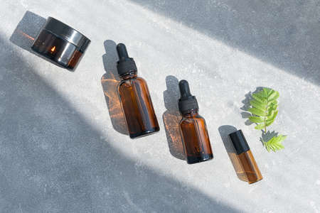Bottles of dark amber glass with essential oil and face cream on a gray concrete background. Natural SPA organic cosmetic. Layout of the beauty salon branding. Flat lay, top view.の写真素材