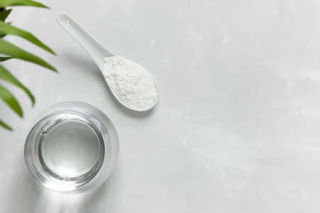 Collagen powder in a spoon and a glass of water on a gray concrete background with a copy space. Extra protein intake.の写真素材