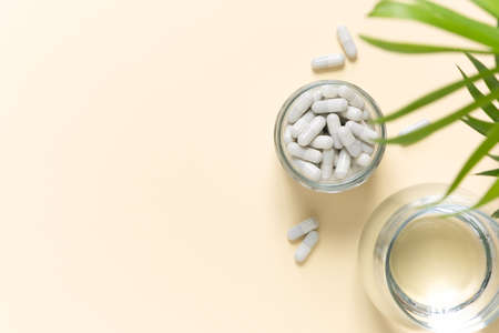 Collagen pills and a glass of water on a beige background with a copy space. Extra protein intake.の写真素材