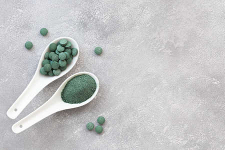 Green algae in powder and pills - chlorella, spirulina a gray background. Healthy green food supplement concept.の写真素材