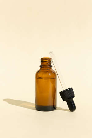 A glass bottle with a pipette for essential oil, lotion or serum on a pastel beige background. Dark amber glass bottle. Layout of the beauty salon brandingの写真素材